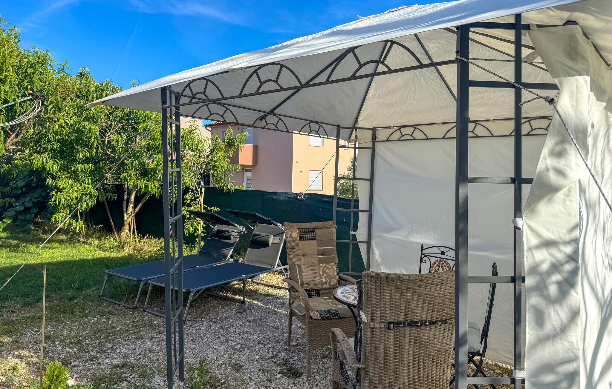 A covered outdoor seating area with a table and chairs, a ladder, and a green tarp on the ground.