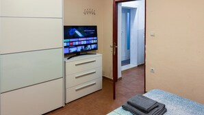 A hotel room with a TV on a stand, a wardrobe, a door leading to another room, and a bed with towels. - 1 bedroom amazing apartment in Pula (Pula)