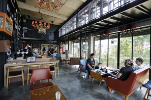 A spacious cafe with high ceilings, large windows, and a mix of seating options including tables and chairs. - Quip Bed & Breakfast (Phuket)