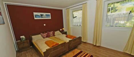 A bedroom with a wooden bed, a nightstand, a window with curtains, and a ceiling light fixture.