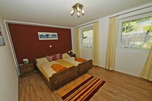 Un dormitorio con cama de madera, una mesita de noche, una ventana con cortinas y una lámpara en el techo.