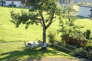 A grassy outdoor area with a tree, a table, two chairs, and a wooden fence. - Apartment Hildegard - Holiday apartment Hildegard (Bizau)
