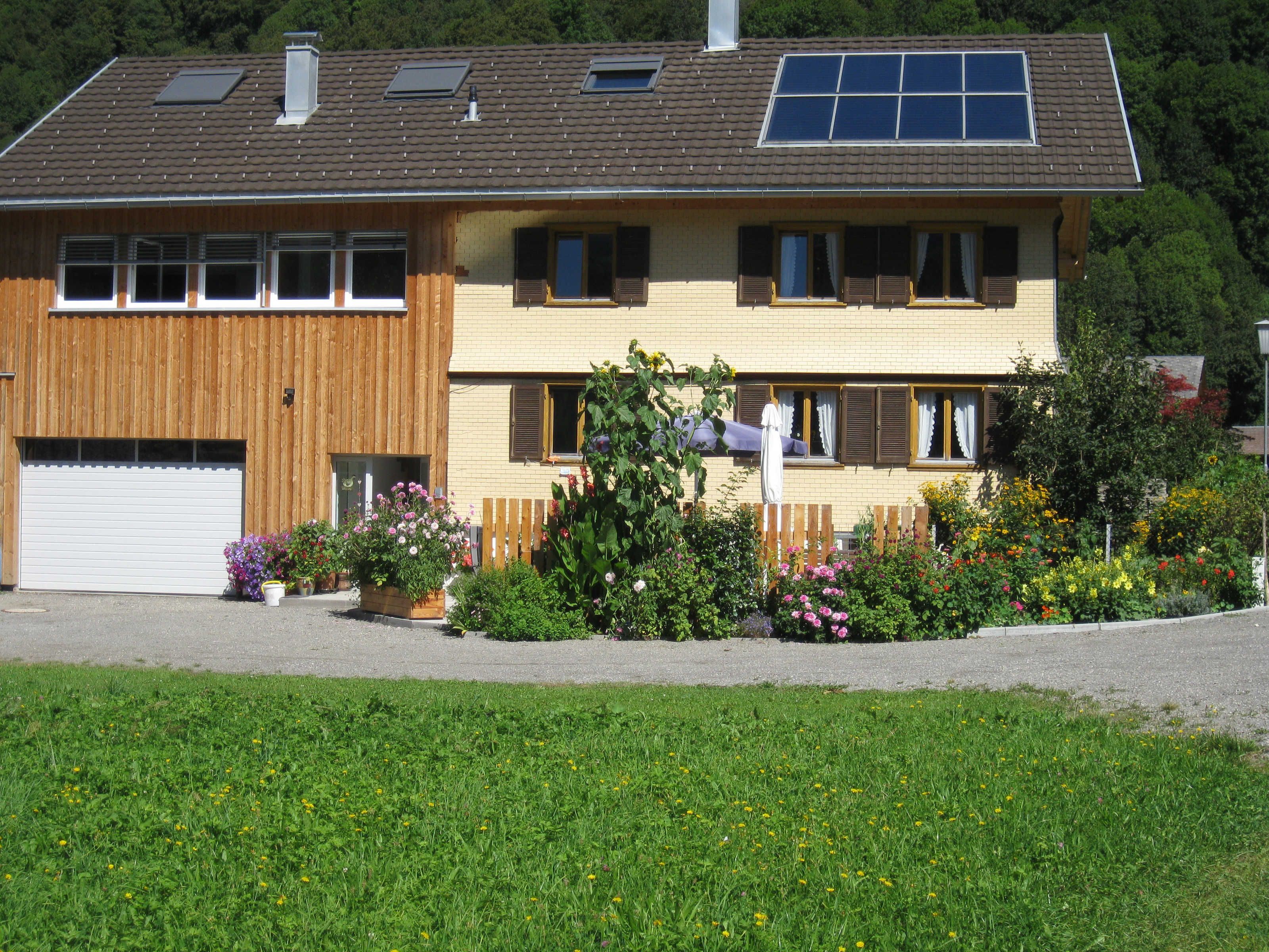Een huis met twee verdiepingen, een garage, zonnepanelen en een tuin met diverse bloemen.