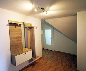 A room with a wooden wardrobe, a small bench, a door leading to a staircase, and a wooden floor.