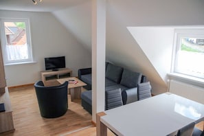 A modern living room with a sofa, a table, a TV, and a window.