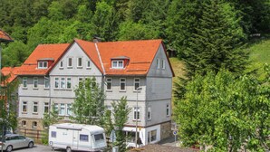 A two-story building with a red-tiled roof, multiple windows, and a parked camper in front. - Apartment Lerbachtal - Apartment Lerbachtal L3 2-6 persons (Osterode am Harz)