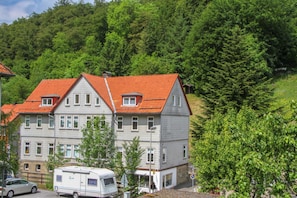 A two-story building with a red-tiled roof, multiple windows, and a parked camper in front.