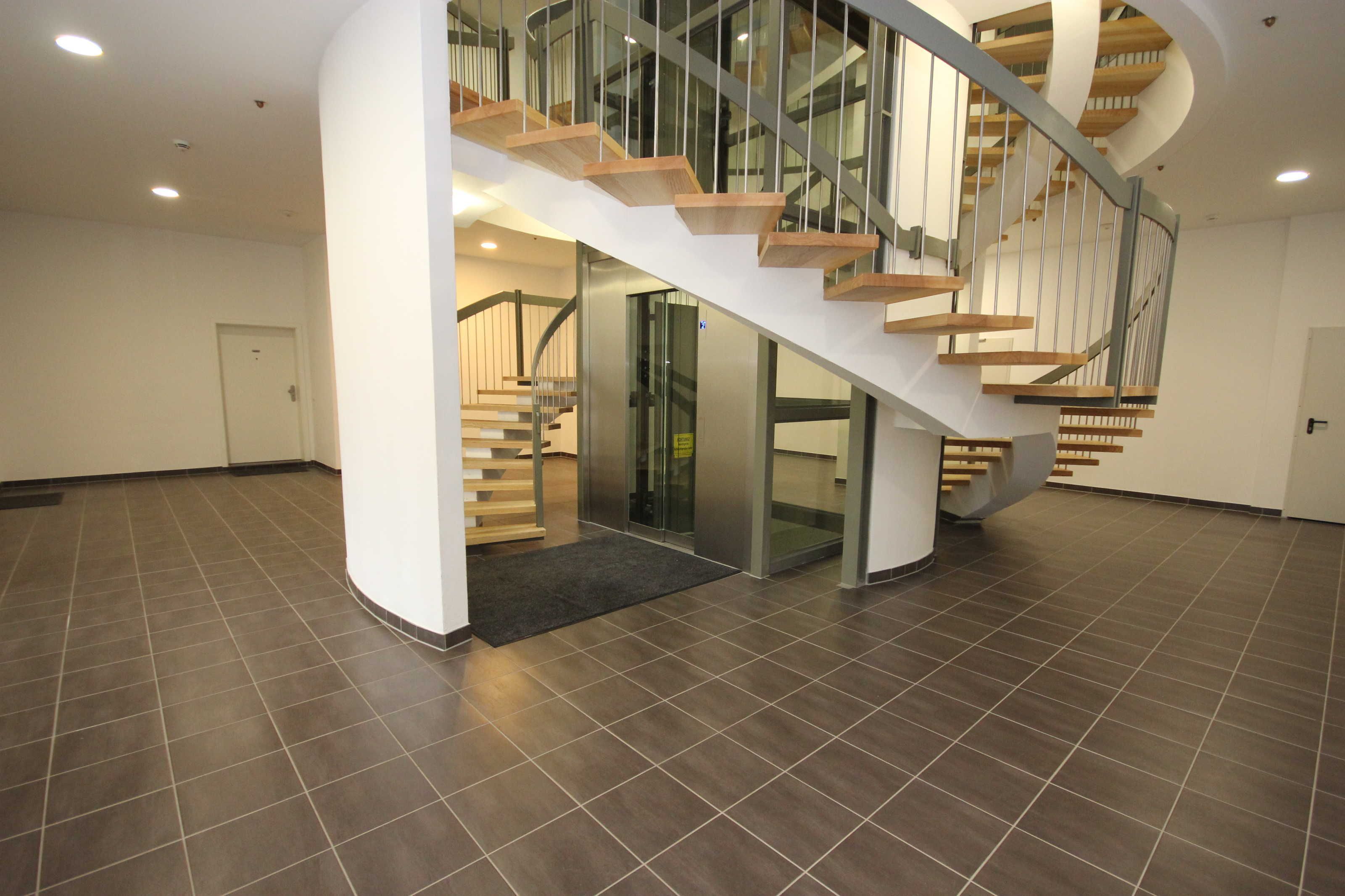 Un intérieur moderne avec un escalier en colimaçon, une entrée avec une porte en verre et un sol carrelé.