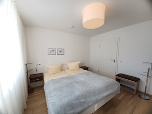 A bedroom with a bed, bedside tables, a bedside lamp, a floor lamp, a door, and two framed pictures on the wall.