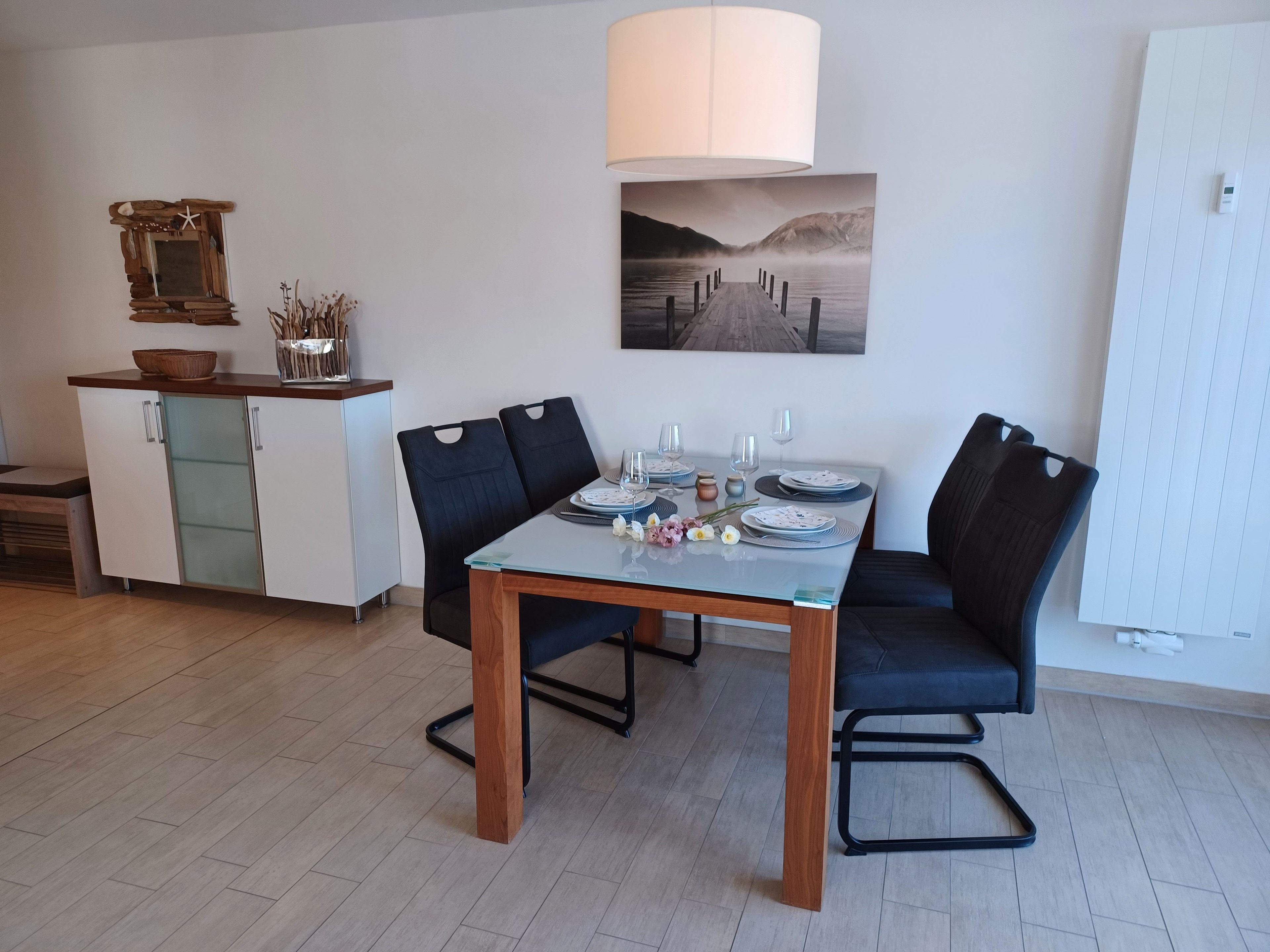 A dining area with a table set for four, two chairs, a cabinet, and a wall-mounted picture.