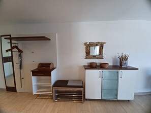 A room with a wooden bench, a white cabinet with glass doors, a mirror, and a hanging coat rack.