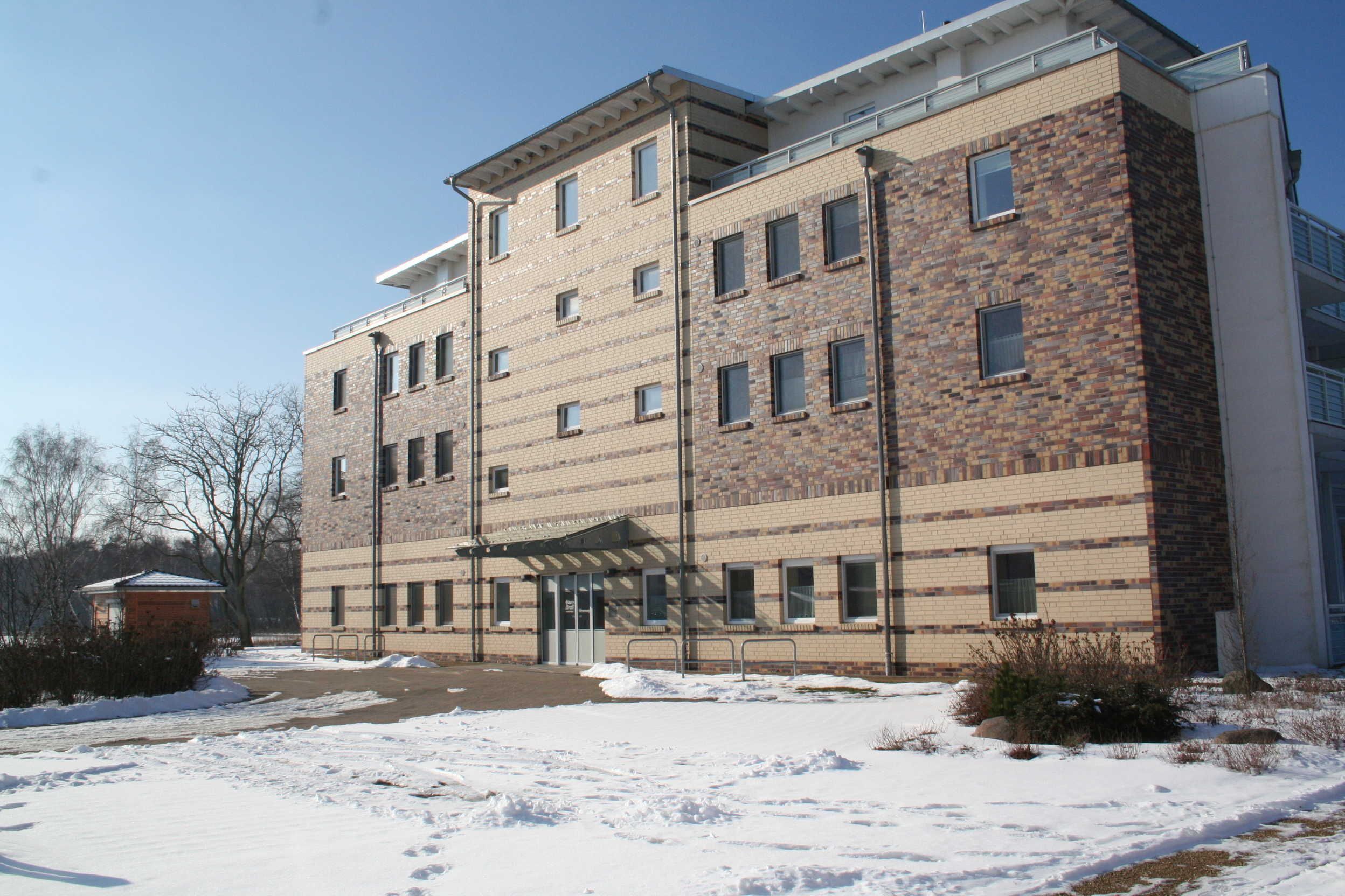 A multi-story building with a brick facade, a covered entrance, and a parking area with snow.