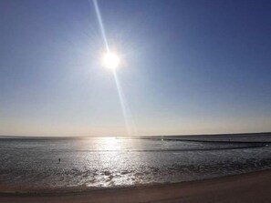 Una playa con cielo despejado y el sol cerca del horizonte.