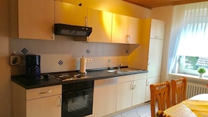 A modern kitchen with a stove, oven, and sink. There is a window with a view of trees and a potted plant on the windowsill. - Fewo Nordlichstraße - Fewo Nordlichtstraße (Norden)