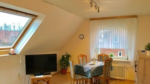 A cozy dining area with a table set for two, a television on a wooden stand, and a potted plant. - Fewo Nordlichstraße - Fewo Nordlichtstraße (Norden)