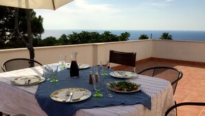 A table set for two with a view of the sea, a blue tablecloth, and a white lace table runner.