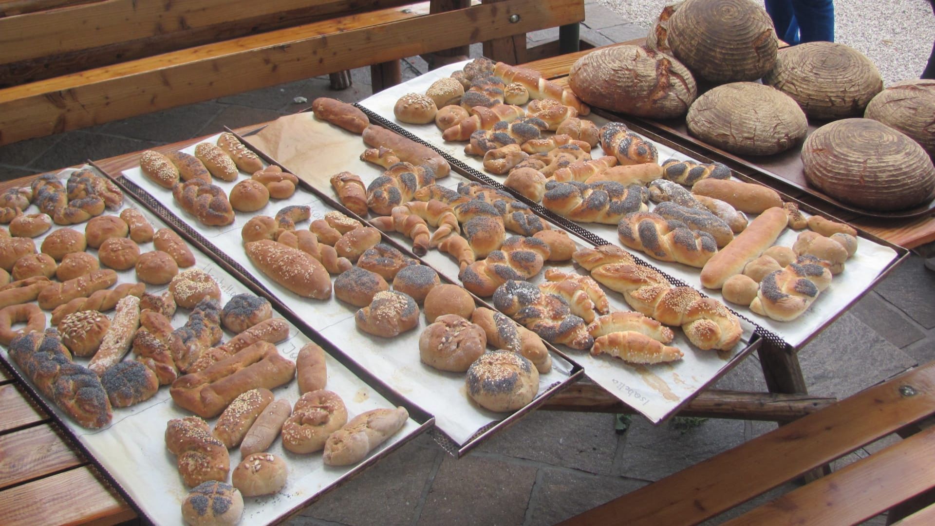 Variedad de productos horneados expuestos en bandejas en un mercado al aire libre.