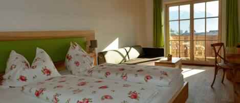 A hotel room with two beds, a sofa, a table, and a view of the mountains.