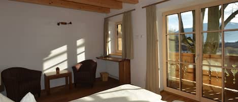 A room with a bed, two chairs, a small table, a window with a view, and a wooden ceiling.