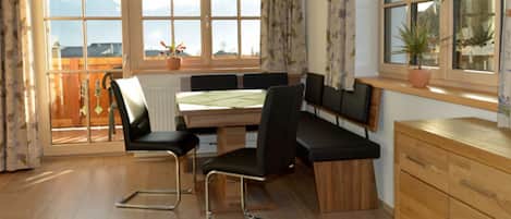 A dining area with a table and chairs, a wooden cabinet, and a view of mountains through large windows.