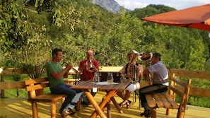 Un grupo de personas sentadas en una mesa de madera al aire libre, con montañas al fondo.
