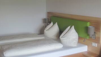 A hotel room with a bed, pillows, a green headboard, a wall-mounted lamp, and a power outlet.