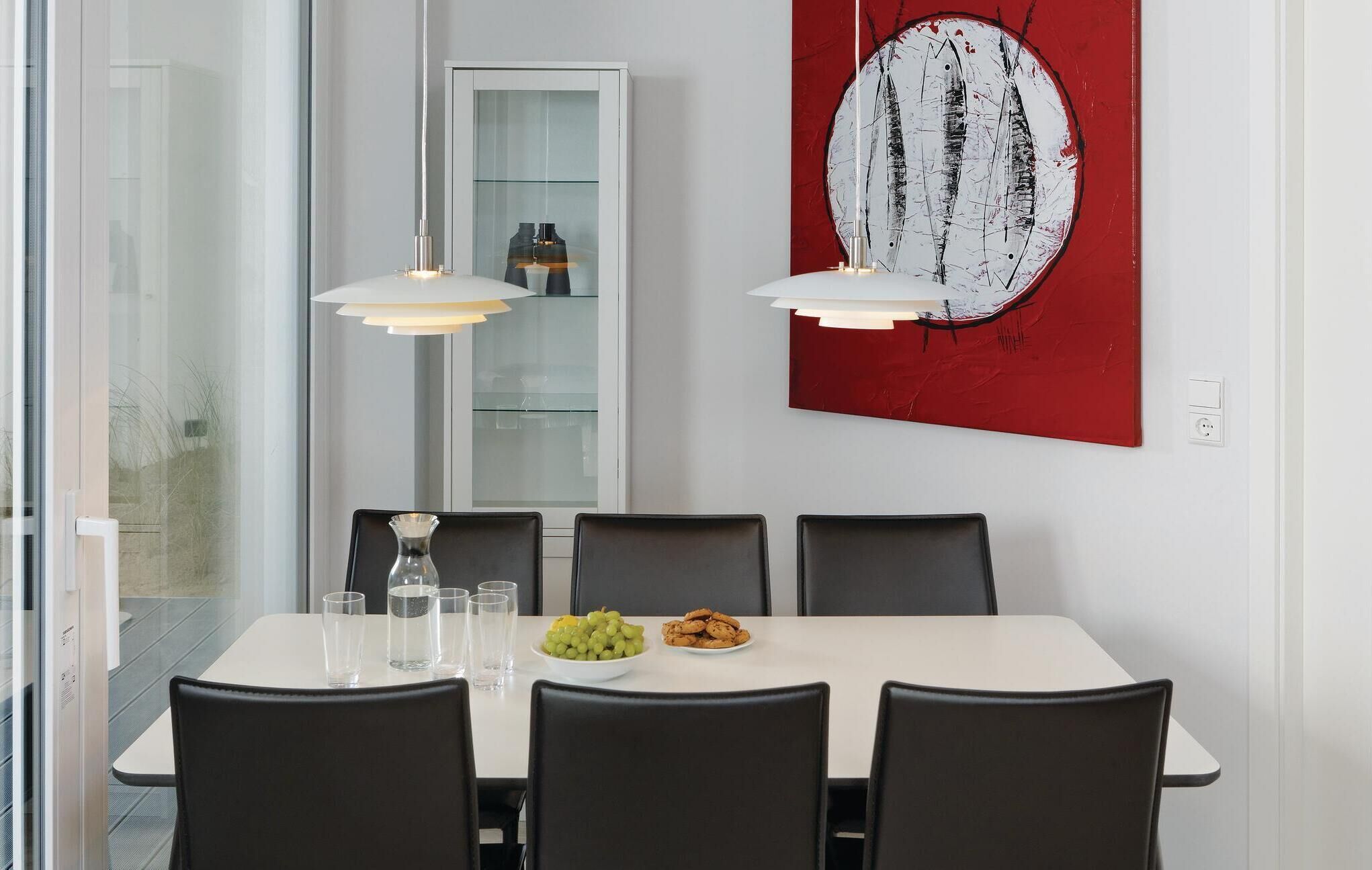 Een moderne eetruimte met een witte tafel, zwarte stoelen en een abstract schilderij in rood.