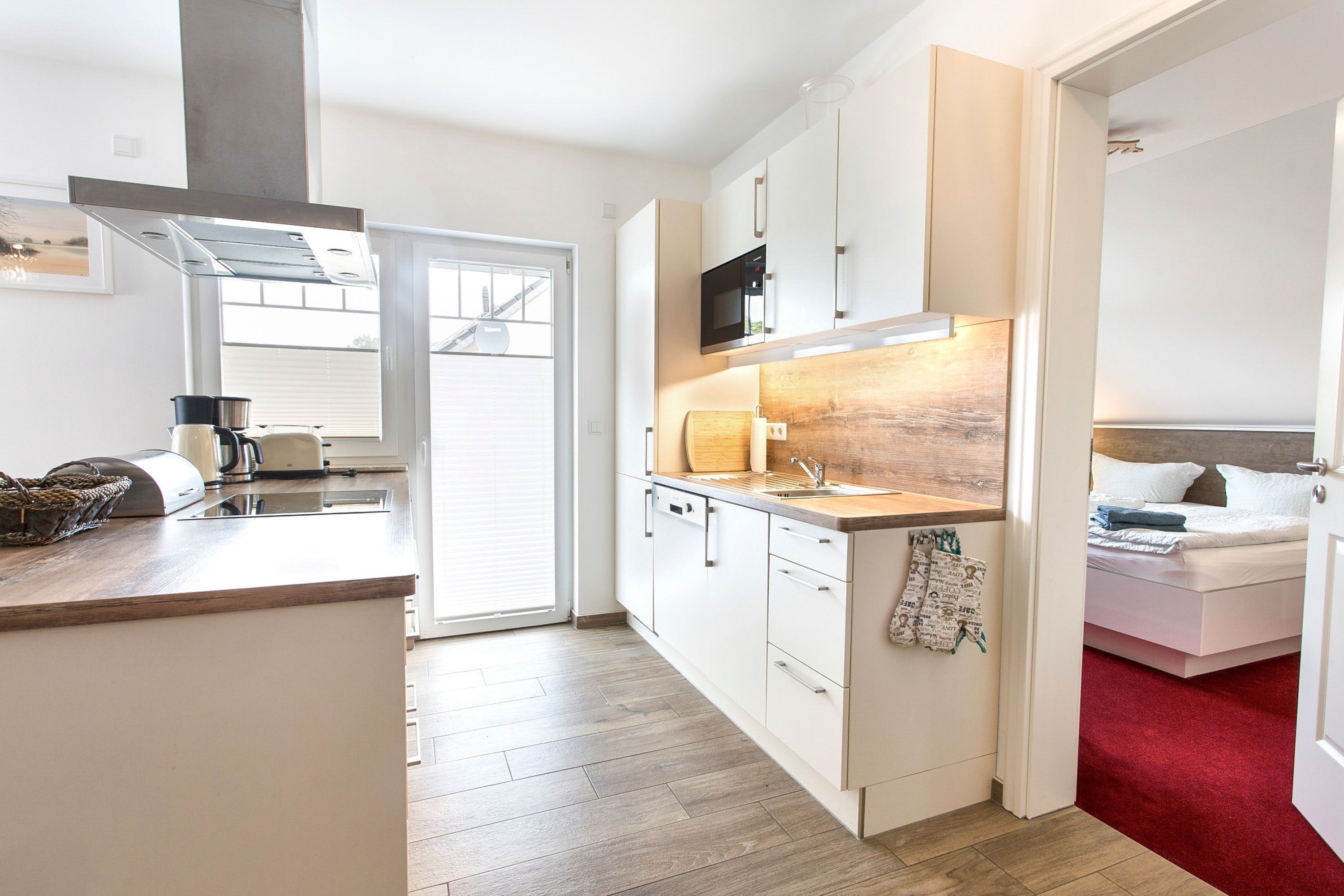 A modern kitchen with a microwave, stove, and sink. There is a wooden countertop and a red carpet leading to a bedroom.