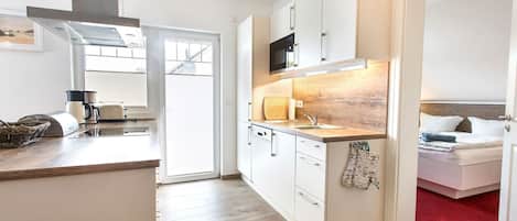 A modern kitchen with a microwave, stove, and sink. There is a wooden countertop and a red carpet leading to a bedroom.