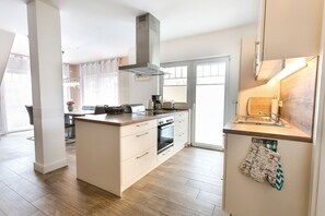 A modern kitchen with a central island, built-in oven, and a stainless steel range hood. - Vacation apartment Rügen - Villa Vier Inselblick (Kröslin OT Freest)