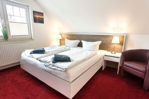 A bedroom with a bed, two bedside tables, a chair, a window, and a radiator. - Vacation apartment Rügen - Villa Vier Inselblick (Kröslin OT Freest)