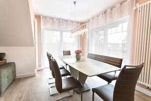 A dining area with a table, chairs, a chandelier, and large windows.