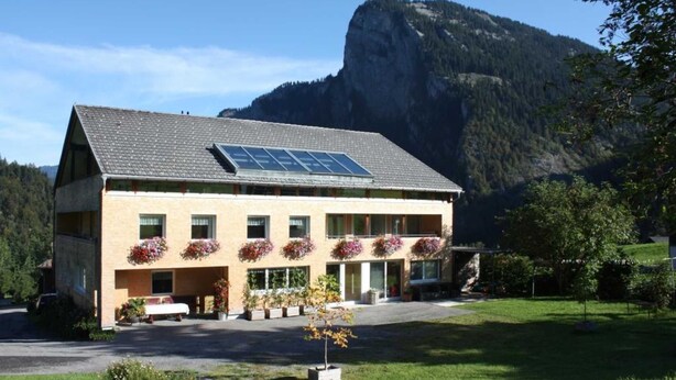 Ein zweistöckiges Gebäude mit einem geneigten Dach, Solaranlagen und Blumenkästen an den Fenstern.