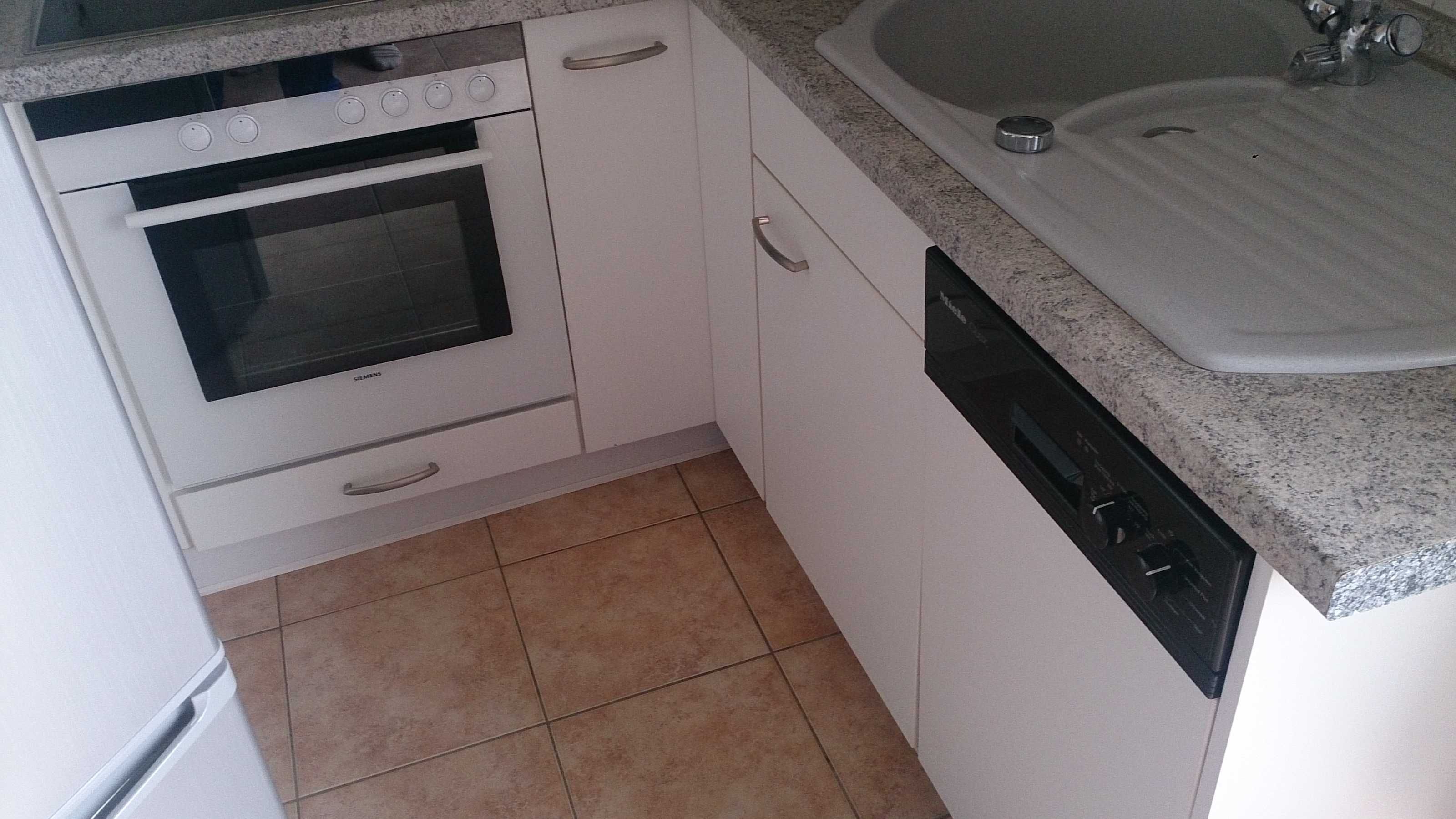 Une cuisine compacte avec des meubles blancs, un four encastré, un lave-vaisselle et un plan de travail en granit.