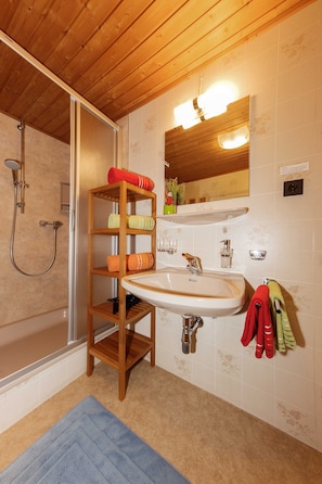 A bathroom with a wooden shelf, a sink, a mirror, and a shower.