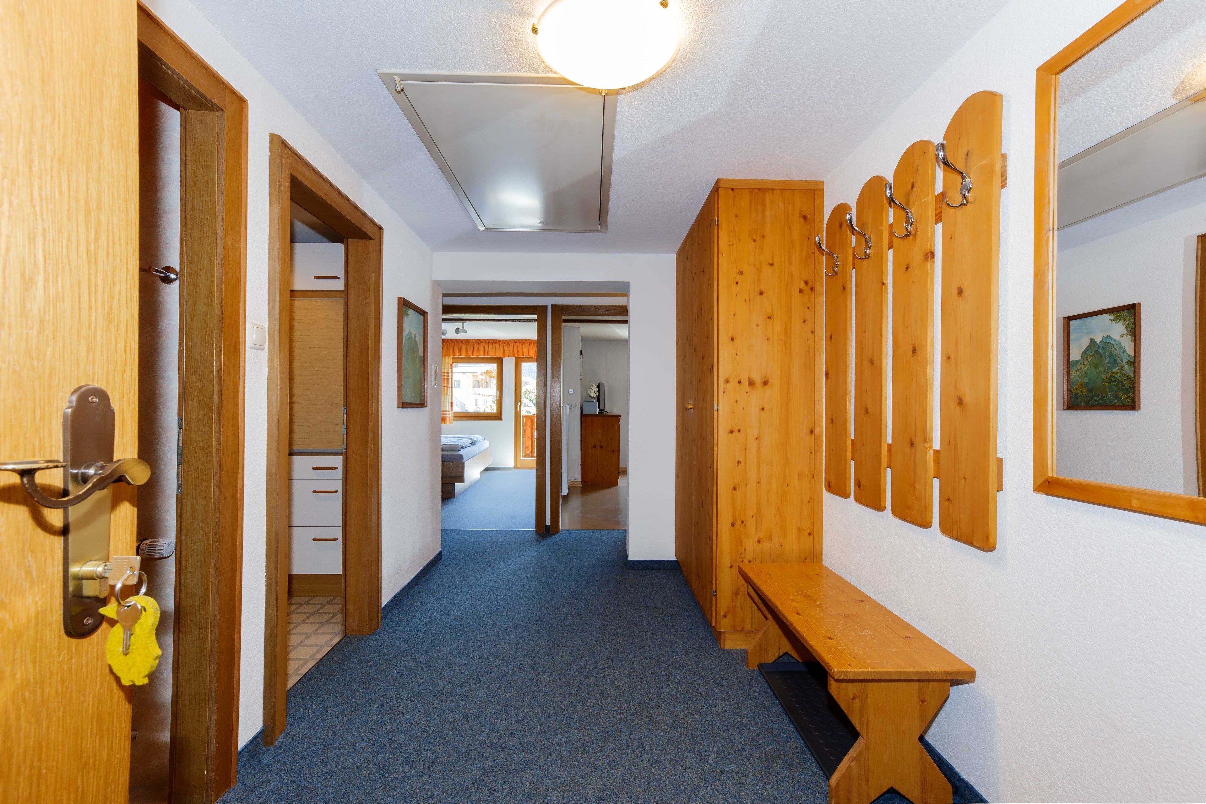 Un couloir avec des portes en bois, un banc et un porte-manteau.