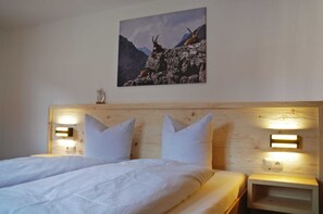 A hotel room with a wooden headboard, two white pillows, a bed with white bedding, and a mountain landscape painting on the wall.