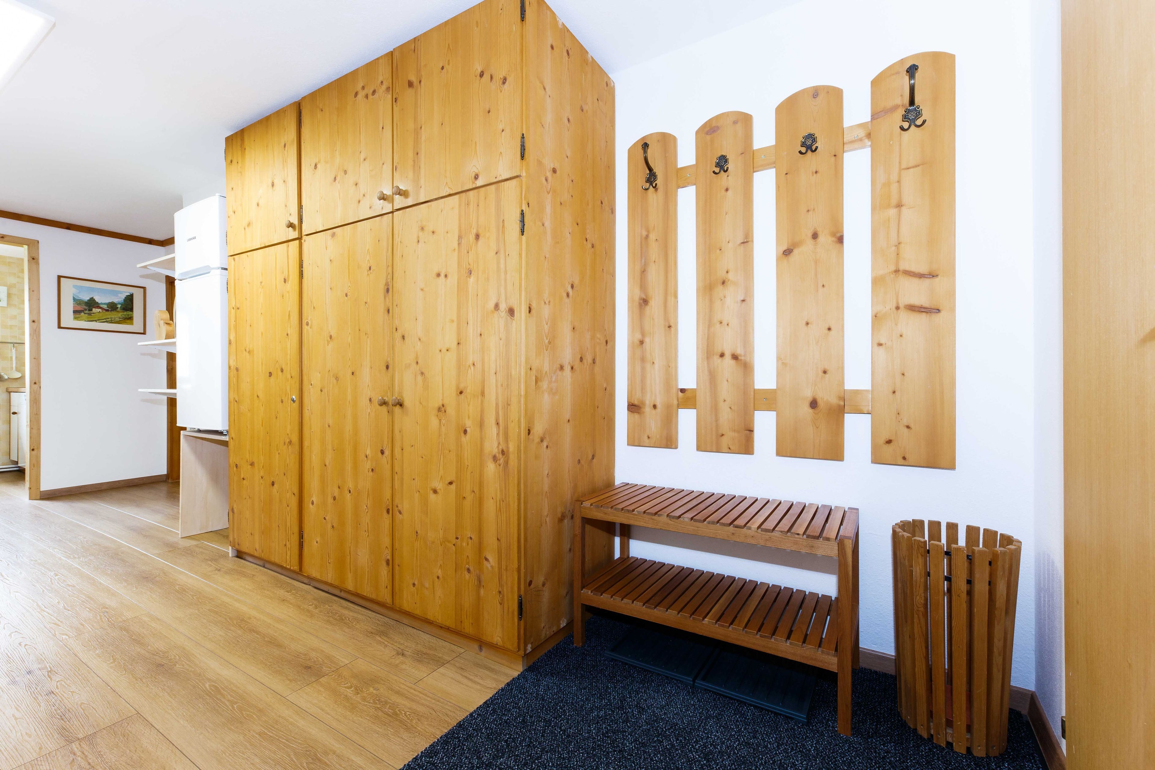 Una habitación con un armario de madera, un banco, un adorno de pared de madera y un cubo de basura.
