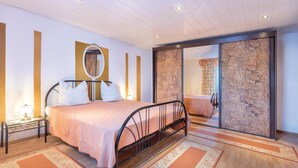 Un dormitorio con cama, mesita de noche, espejo y puerta corredera que da a otra habitación.