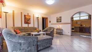 Una sala de estar con sofá, sillón y mesa de centro, una cocina al fondo y un comedor con mesa y sillas.