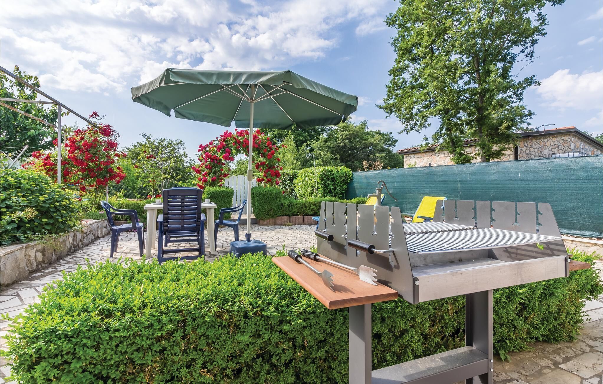 An outdoor patio with a grill, chairs, and an umbrella.