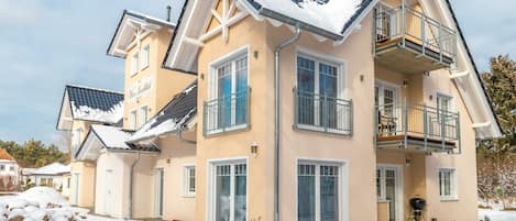 A multi-story residential building with a balcony, a garage, and a snow-covered roof.