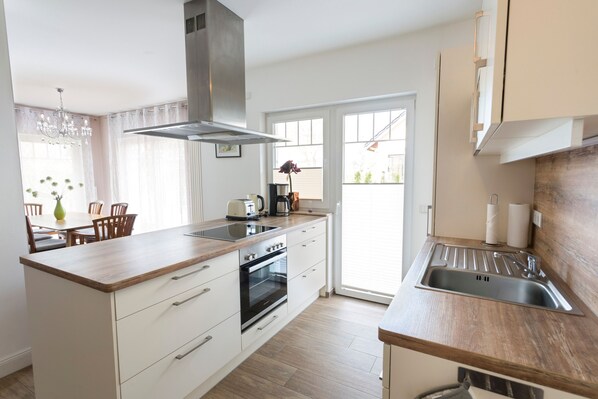 A modern kitchen with a central island, built-in oven, and a large window. - Apartment Ruden - Villa Vier Inselblick (Kröslin OT Freest)