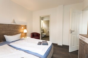 A hotel room with a bed, a chair, a desk, a wardrobe, and a bathroom visible through an open door. - Apartment Ruden - Villa Vier Inselblick (Kröslin OT Freest)