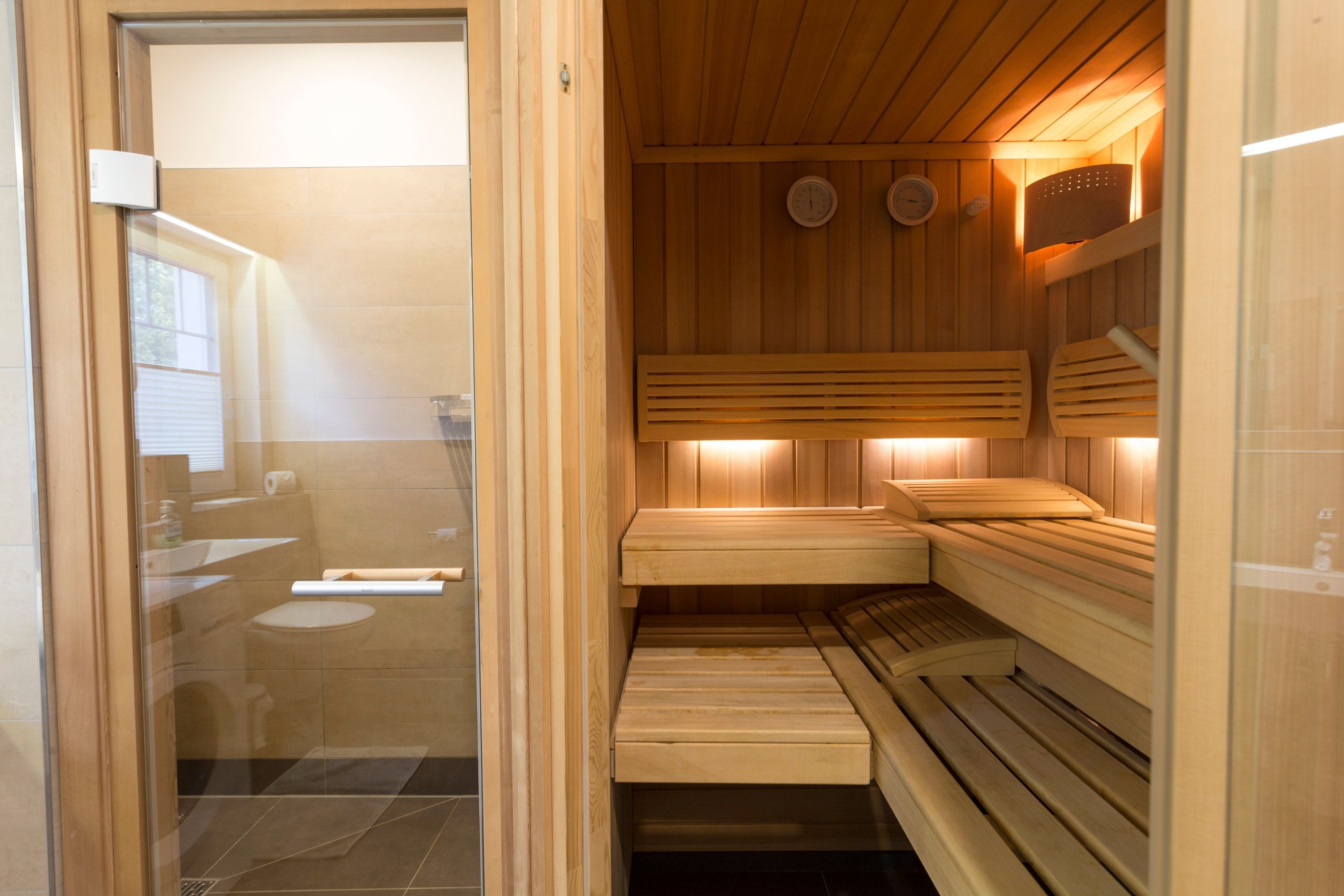 A sauna room with wooden benches and a glass door leading to a bathroom.