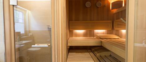 A sauna room with wooden benches and a glass door leading to a bathroom.