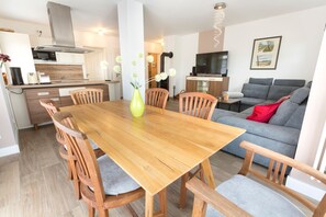 A modern kitchen with a dining area, grey sofa, and a TV. - Apartment Ruden - Villa Vier Inselblick (Kröslin OT Freest)