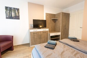 A bedroom with two beds, a TV, a wardrobe, and a red chair. - Apartment Ruden - Villa Vier Inselblick (Kröslin OT Freest)