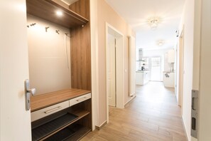 A hallway with a wooden bench, a white door, and a kitchen area in the distance. - Apartment Ruden - Villa Vier Inselblick (Kröslin OT Freest)