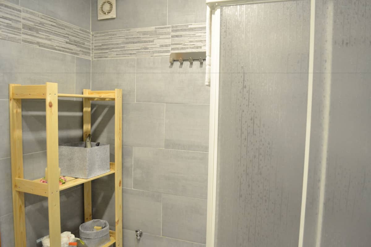 Un baño con paredes de azulejos grises, un estante de madera y una zona de ducha.